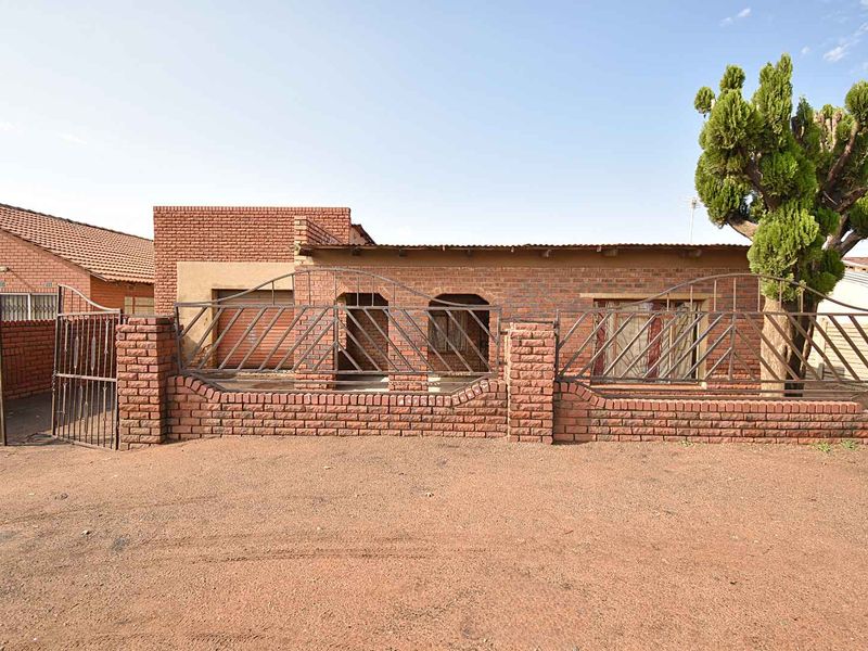 Front elevation of a face brick house featuring a secure wrought iron perimeter fence and gate with a paved driveway area.