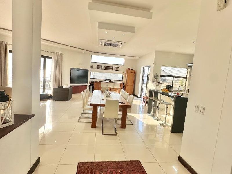 Spacious open-plan living and dining area featuring tiled floors, a modern kitchen island with breakfast bar, and integrated ducted air conditioning.