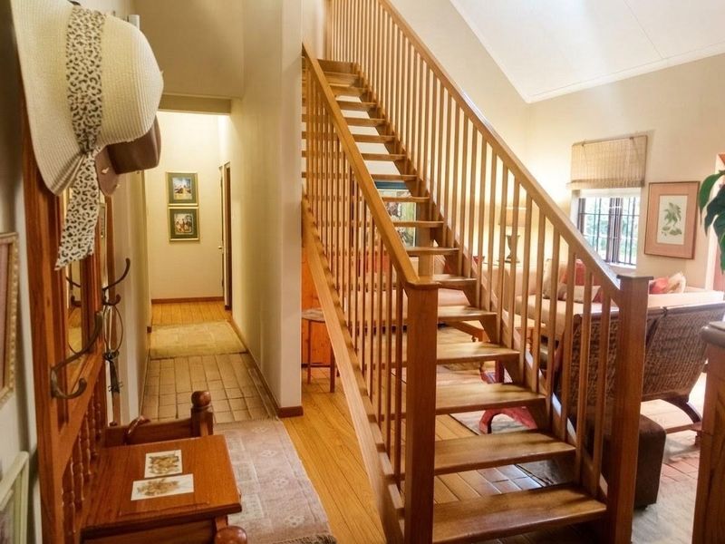 A bright hallway featuring a prominent wooden staircase with a matching balustrade, leading towards an open living area with hardwood flooring.