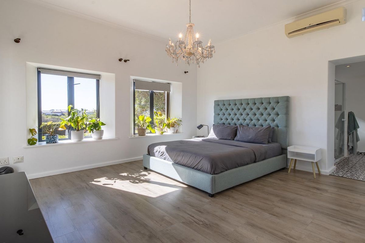 Spacious bedroom featuring light-toned laminate flooring, recessed windows with natural light, a split-system air conditioner, and direct access to an en-suite bathroom.