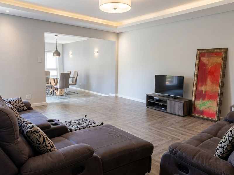 Spacious open-plan living and dining area featuring modern herringbone flooring, recessed ceiling lighting, and elegant cove lighting throughout the space.