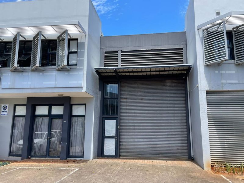 Modern mixed-use commercial unit featuring a large roller shutter door, aluminium window frames with louvre shutters, and a paved frontage.