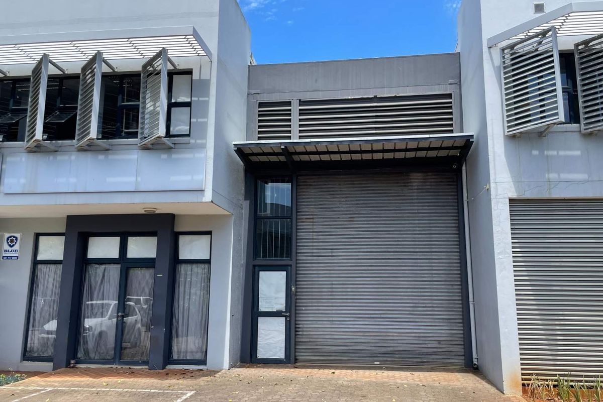 Modern mixed-use commercial unit featuring a large roller shutter door, aluminium window frames with louvre shutters, and a paved frontage.
