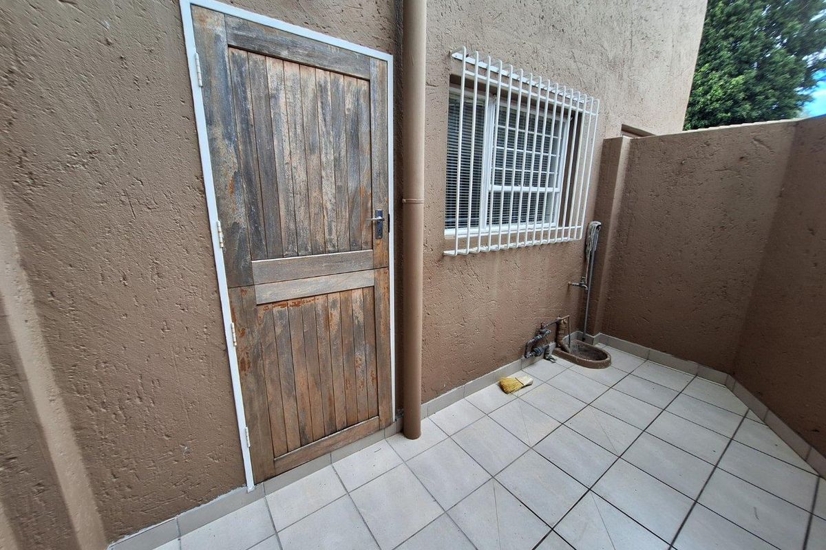 A rear exterior courtyard area featuring tiled flooring, a security-barred window, and an external water point with a drainage basin.
