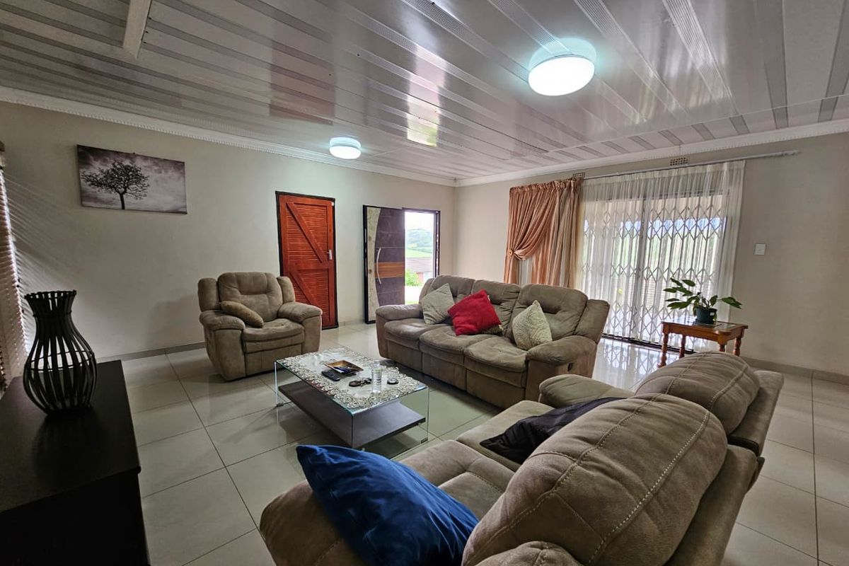 Spacious living room featuring tiled flooring, a panelled ceiling, and a sliding glass door with a security gate providing access to the exterior.