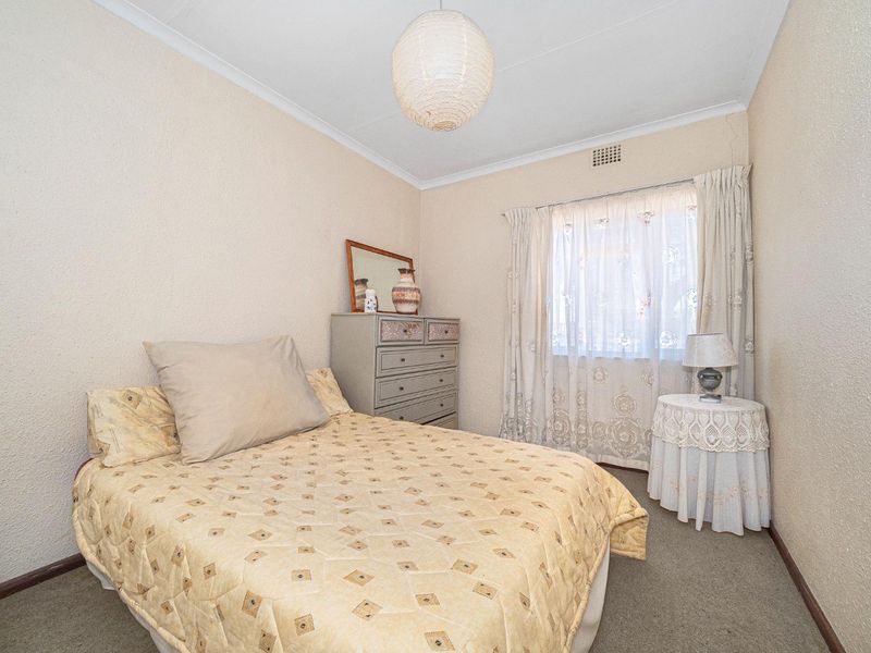 A compact bedroom featuring carpeted flooring, a ceiling vent, and coving, with visible wall plaster cracking requiring maintenance.