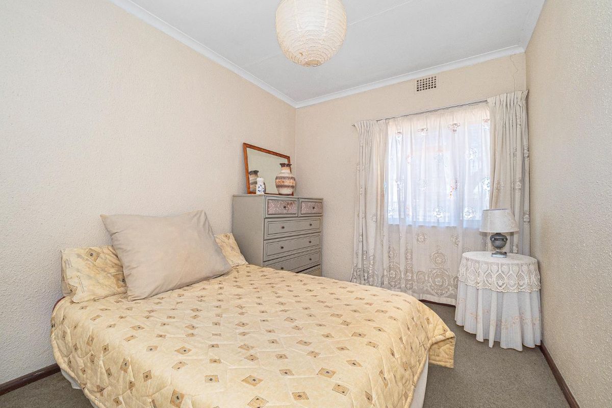 A compact bedroom featuring carpeted flooring, a ceiling vent, and coving, with visible wall plaster cracking requiring maintenance.