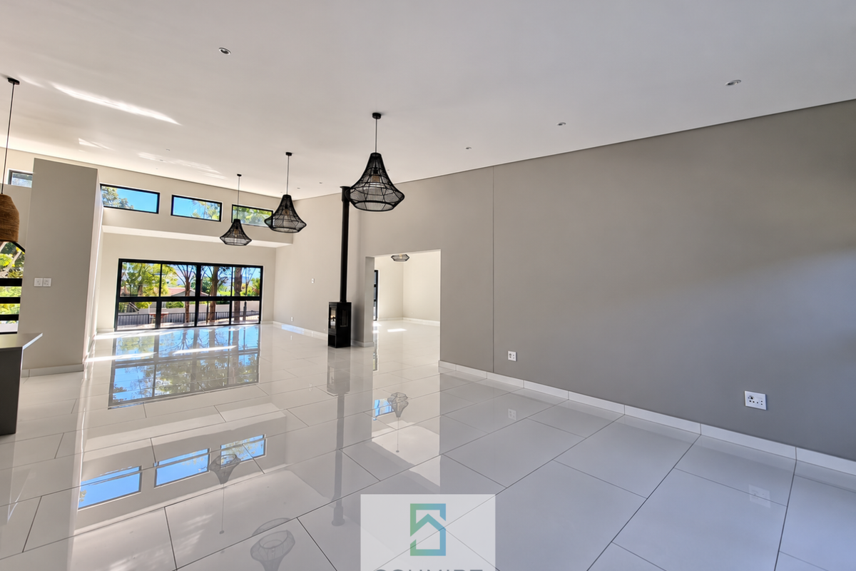 Spacious, modern open-plan living area featuring high ceilings, polished porcelain tiles, a sleek freestanding fireplace, and large windows providing abundant natural light.
