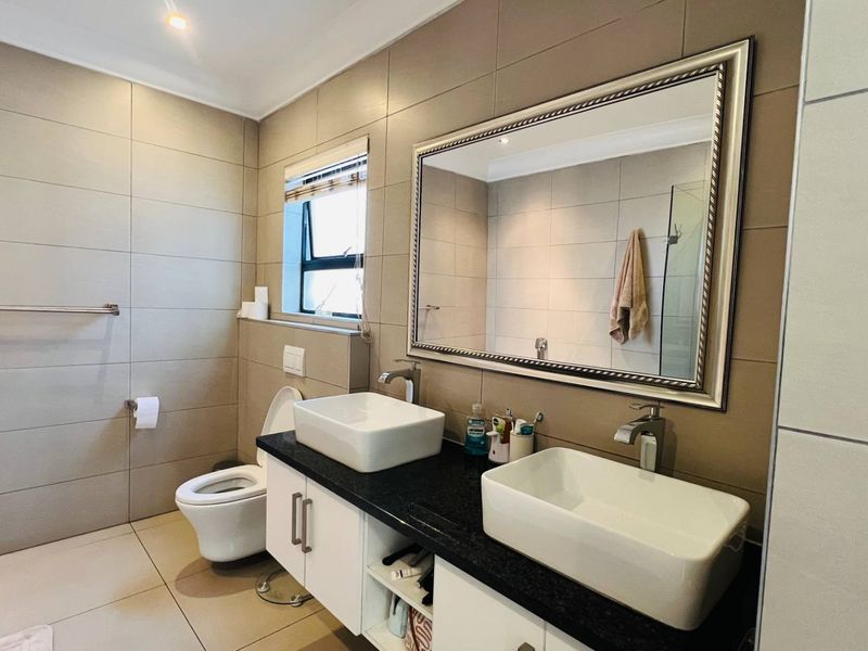 Modern bathroom featuring a double vanity with vessel sinks, wall-mounted toilet, and neutral floor-to-ceiling wall tiles.