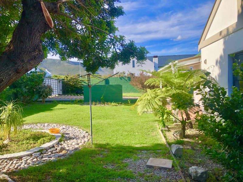 A private rear garden featuring a well-maintained lawn, stone landscaping borders, and a boundary wall with mountain views in the background.