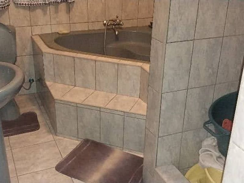A dated bathroom featuring a corner bathtub, pedestal basin, and toilet with neutral wall and floor tiling.