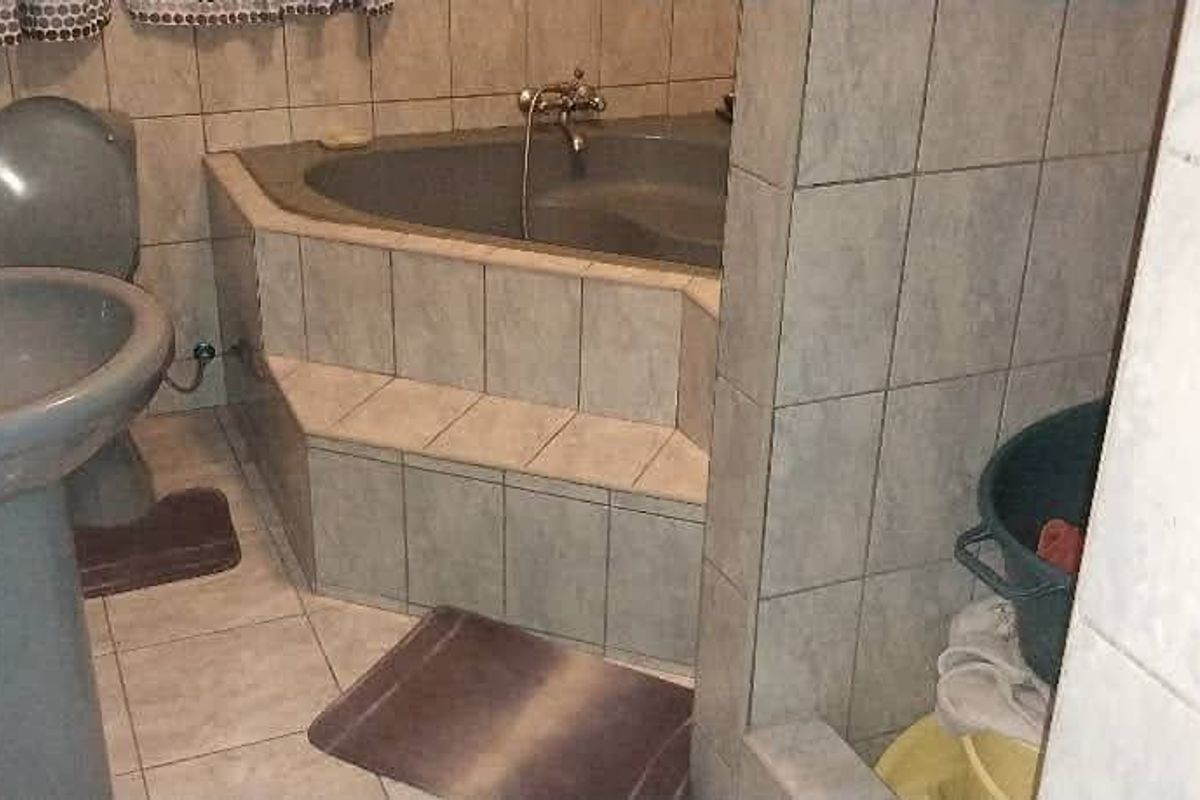 A dated bathroom featuring a corner bathtub, pedestal basin, and toilet with neutral wall and floor tiling.