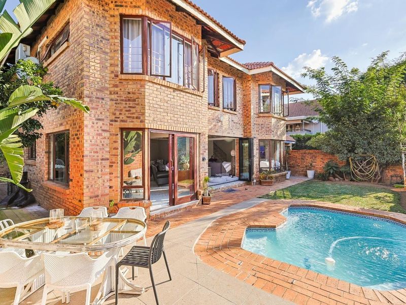 Rear view of a double-storey face brick house featuring a swimming pool, paved patio area, and large stacking doors leading to the interior.