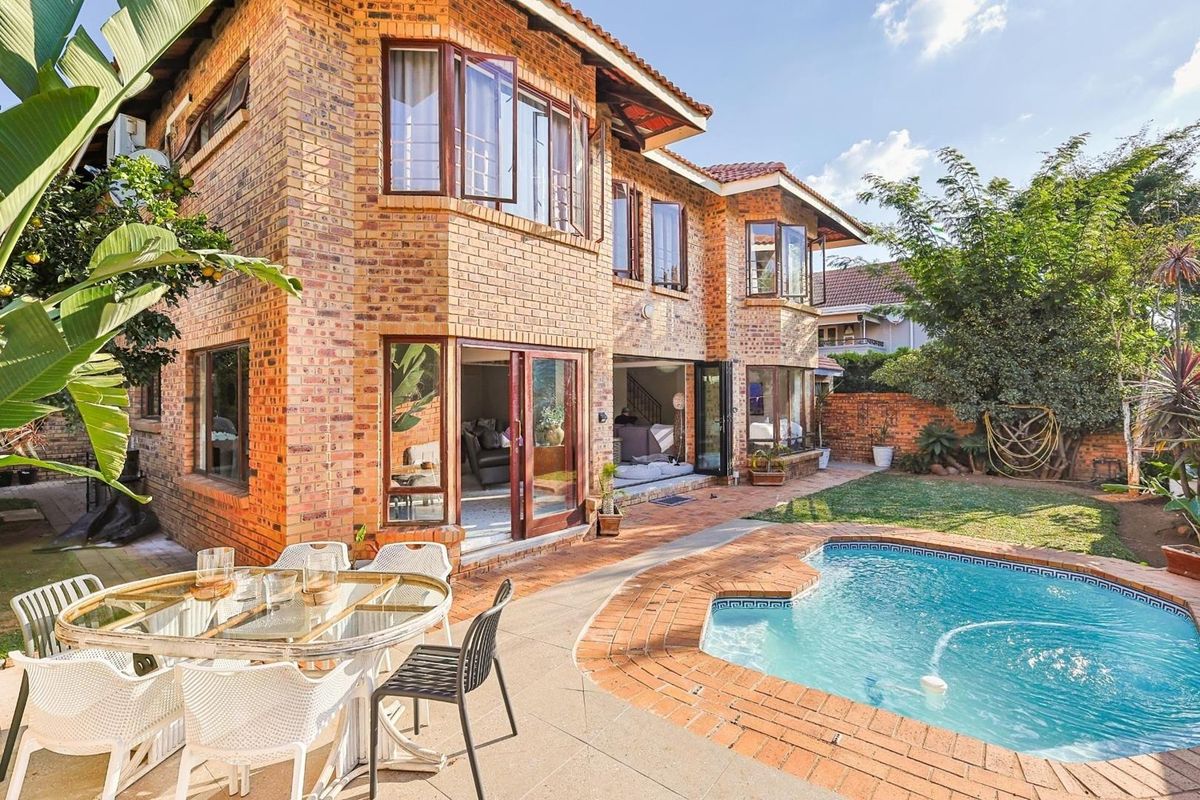 Rear view of a double-storey face brick house featuring a swimming pool, paved patio area, and large stacking doors leading to the interior.