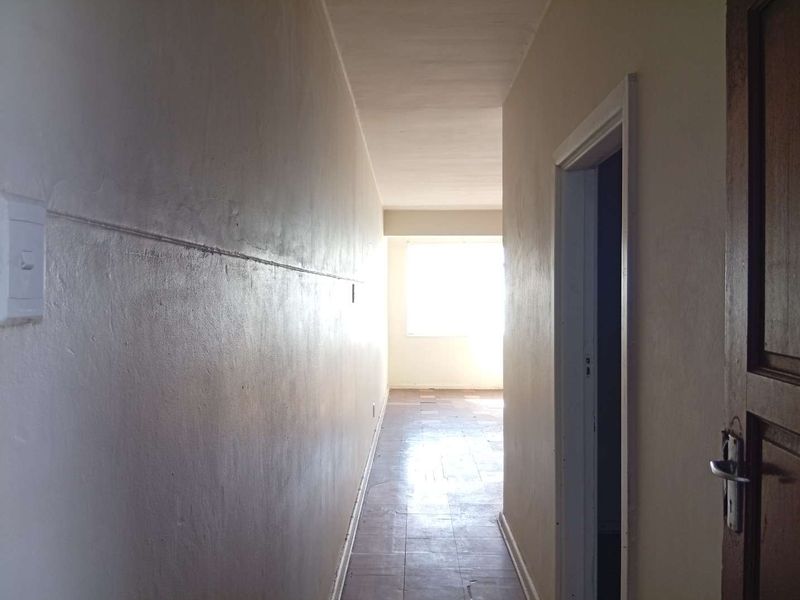 A vacant hallway featuring tiled flooring and neutral walls, leading towards a bright window at the end of the passage.