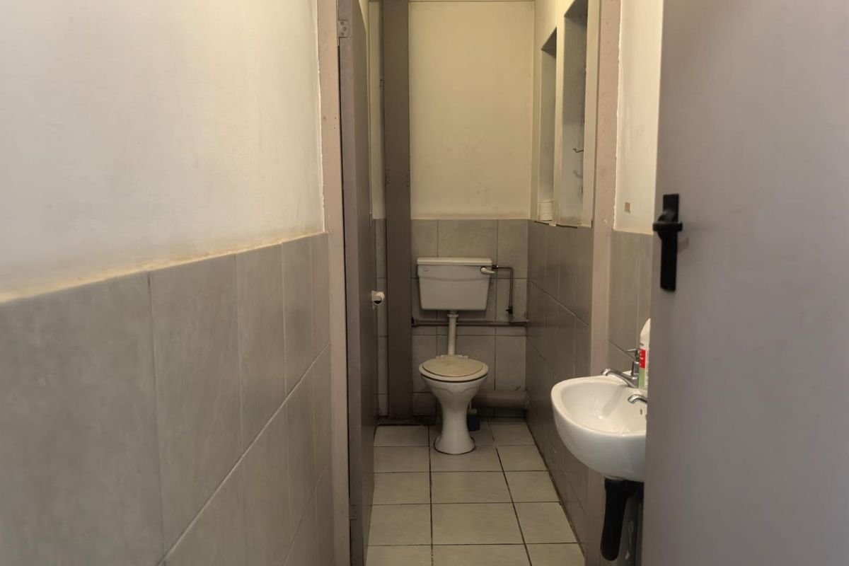 A compact, functional bathroom featuring a standard toilet, wall-mounted basin, and neutral ceramic tiling throughout, requiring cosmetic updates to improve its overall condition.