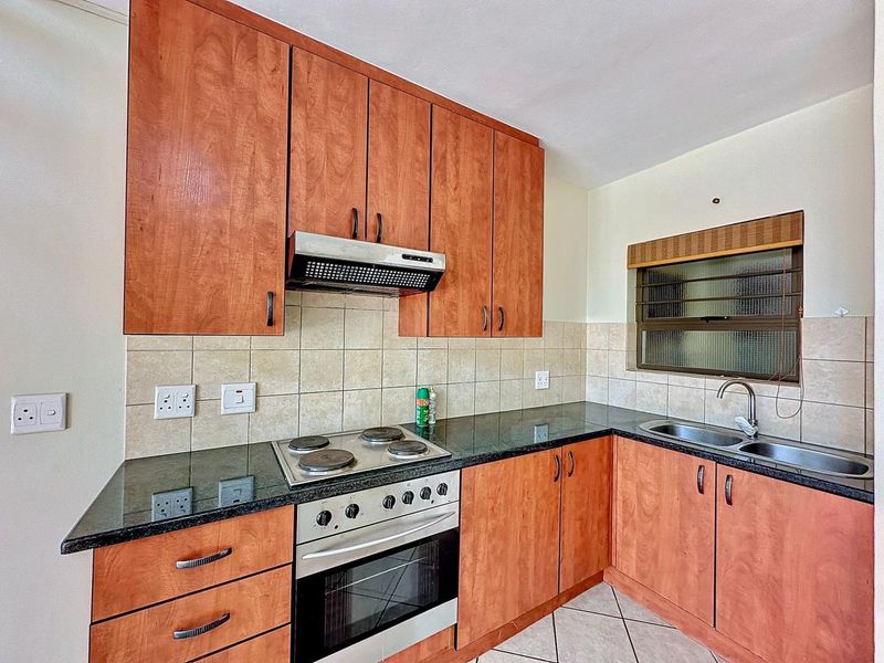 A functional kitchen featuring wood-finish cabinetry, granite countertops, a built-in electric stove with extractor fan, and a double bowl sink.
