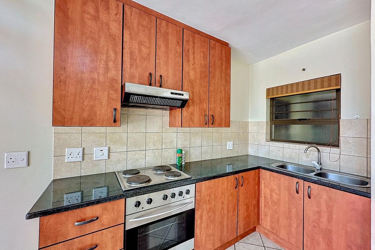 A functional kitchen featuring wood-finish cabinetry, granite countertops, a built-in electric stove with extractor fan, and a double bowl sink.