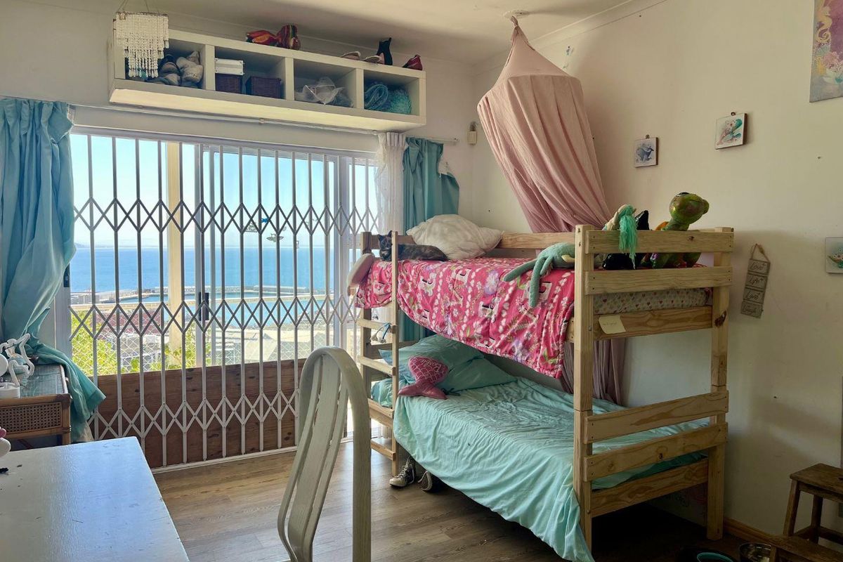 Bedroom featuring laminate flooring, built-in shelving, and a sliding glass door with security gate providing access to a balcony with ocean views.