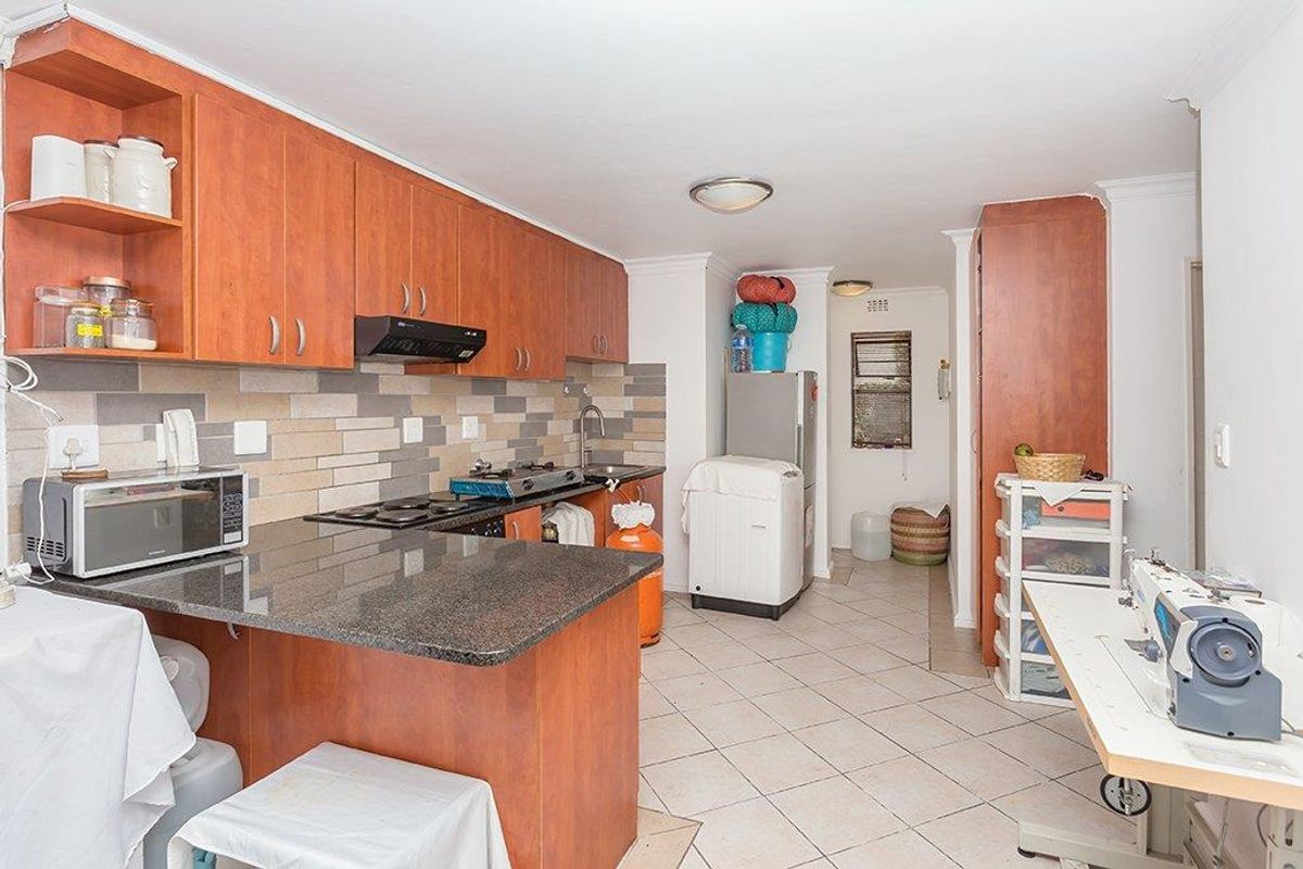 A functional kitchen featuring wood-veneer cabinetry, granite countertops, a built-in hob, and a tiled backsplash, leading into a utility area.