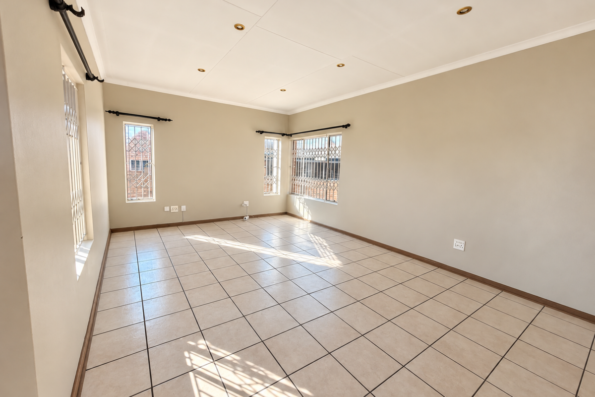 A bright, empty living room featuring neutral tiled flooring, recessed downlighting, and security bars on the windows.