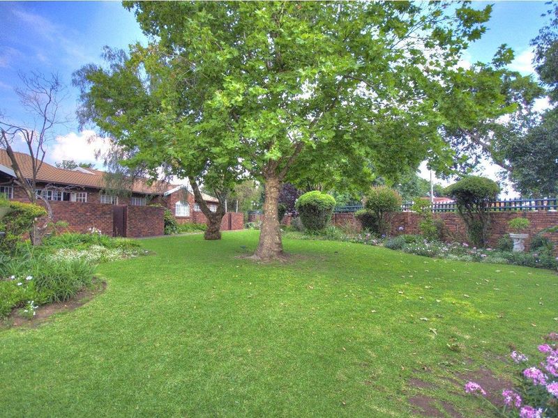 A well-maintained private garden featuring a lush green lawn, mature trees, and established brick boundary walls, providing a peaceful outdoor space.