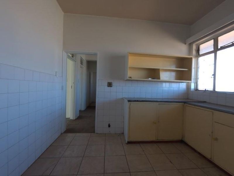 An empty, dated kitchen featuring tiled flooring, tiled splashbacks, and original built-in cabinetry, offering a blank canvas for renovation.