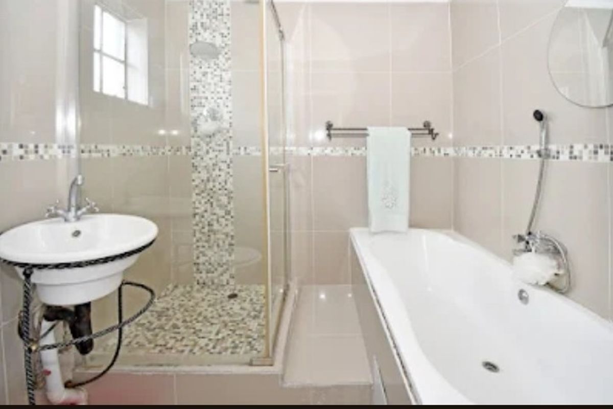 A functional bathroom featuring a pedestal basin, a built-in bathtub, and a separate shower enclosure with decorative mosaic tile accents.