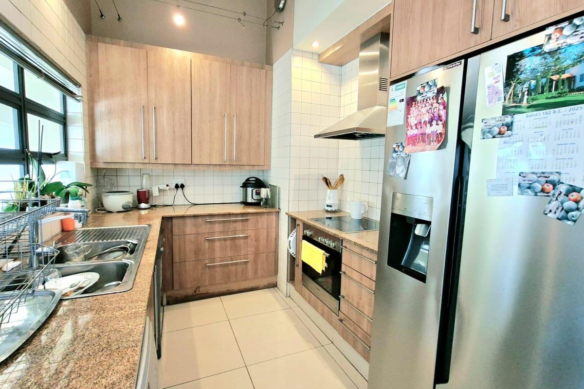 A functional kitchen featuring light wood cabinetry, granite countertops, tiled splashbacks, and integrated stainless steel appliances including an oven and extractor fan.