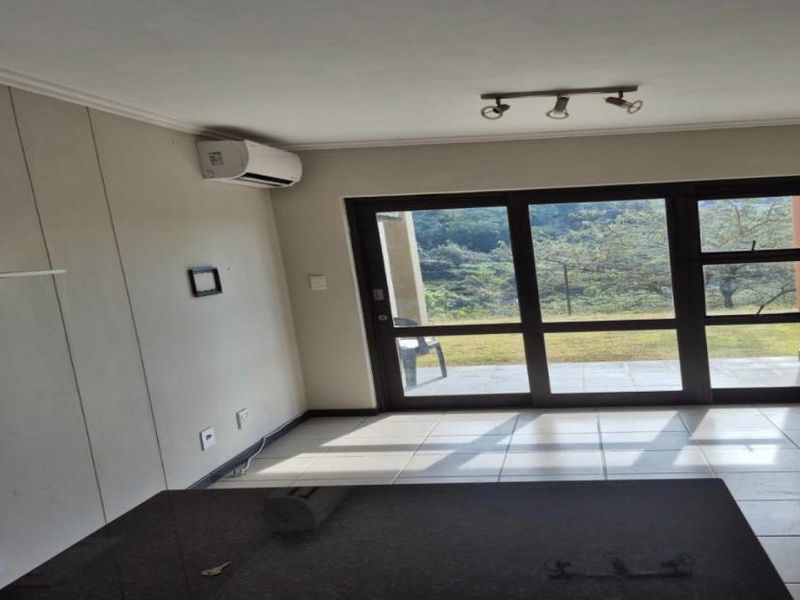 An empty living room featuring tiled flooring, an air conditioning unit, and large sliding glass doors providing access to an outdoor area.