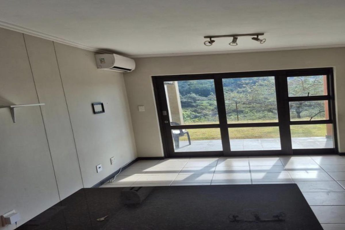 An empty living room featuring tiled flooring, an air conditioning unit, and large sliding glass doors providing access to an outdoor area.