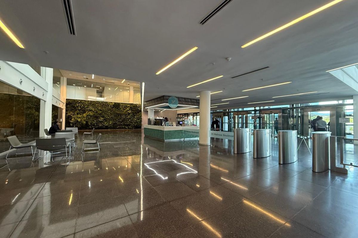 Modern office building lobby featuring a reception desk, secure turnstile access, polished stone floors, and a prominent vertical garden wall.
