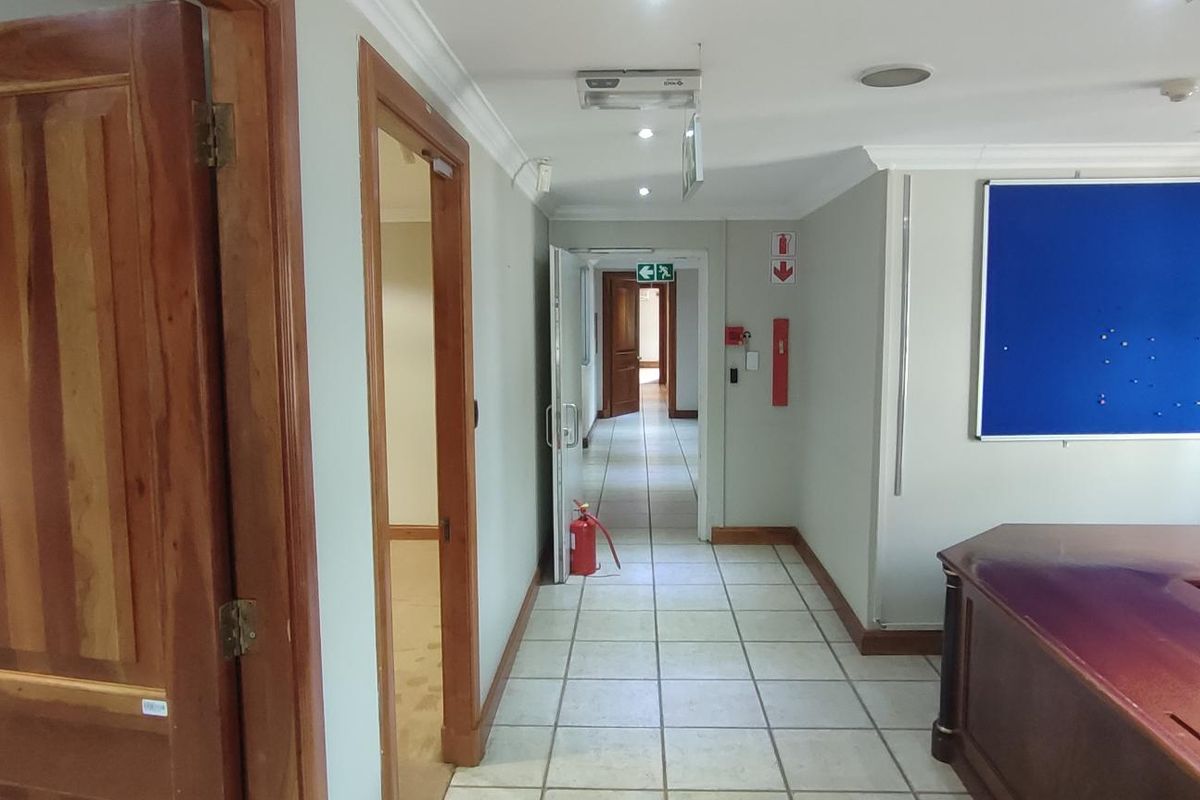 A functional office hallway featuring tiled flooring, recessed lighting, and integrated fire safety equipment, providing access to multiple office rooms.
