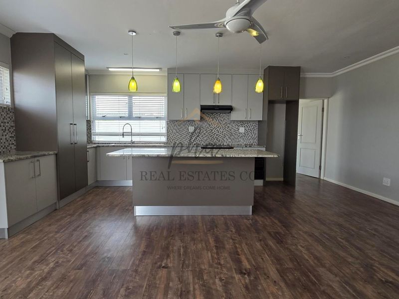 Modern open-plan kitchen featuring a central island, granite countertops, mosaic backsplash, and sleek built-in cabinetry with integrated appliances.