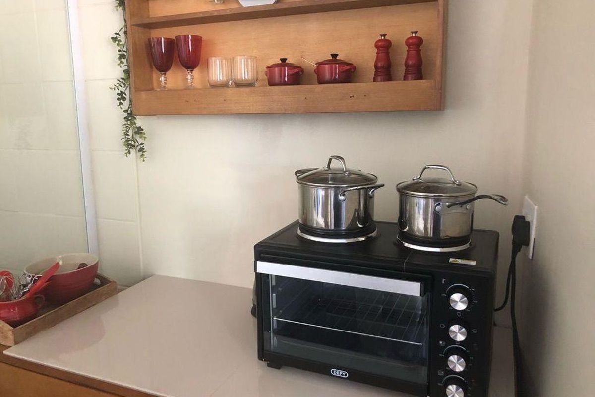A compact kitchen prep area featuring a countertop, wall-mounted wooden shelving, and a portable electric oven with integrated stovetop burners.
