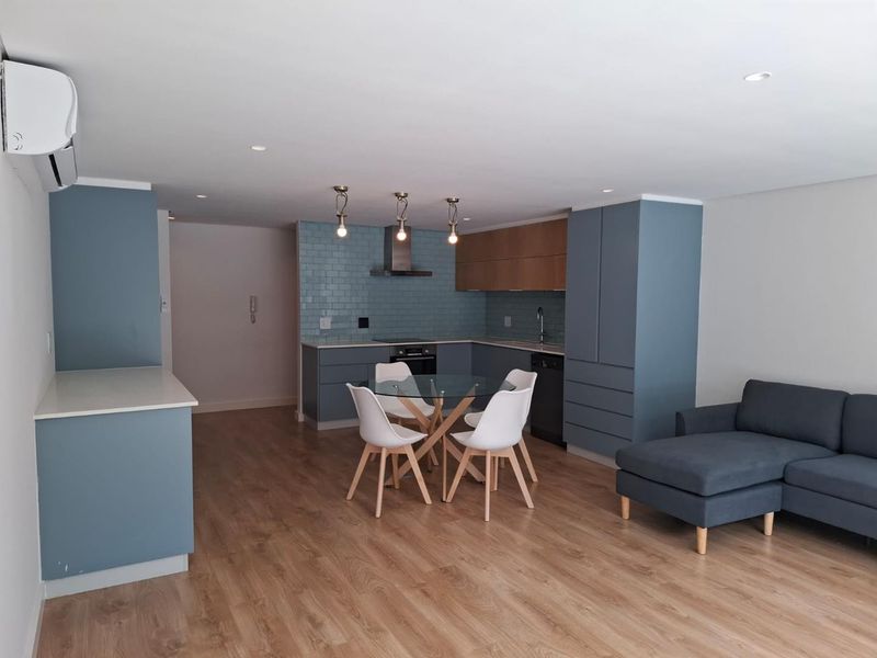 Modern open-plan living area featuring a contemporary kitchen with blue cabinetry, subway tile backsplash, and integrated appliances, seamlessly flowing into the dining and lounge space.