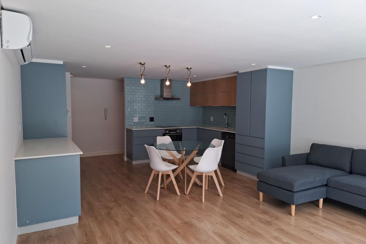 Modern open-plan living area featuring a contemporary kitchen with blue cabinetry, subway tile backsplash, and integrated appliances, seamlessly flowing into the dining and lounge space.