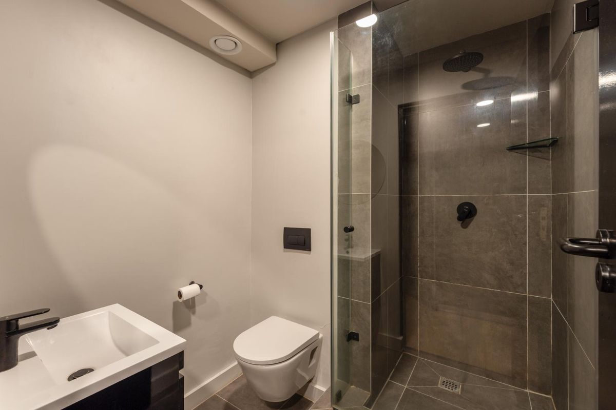 Modern bathroom featuring a glass-enclosed shower with rain head, wall-mounted toilet, and a sleek vanity basin with contemporary finishes.