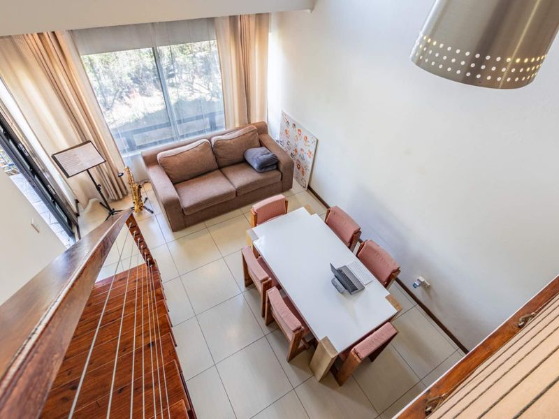 An open-plan living and dining area featuring tiled floors, a wooden staircase with cable balustrades, and large sliding doors providing natural light.