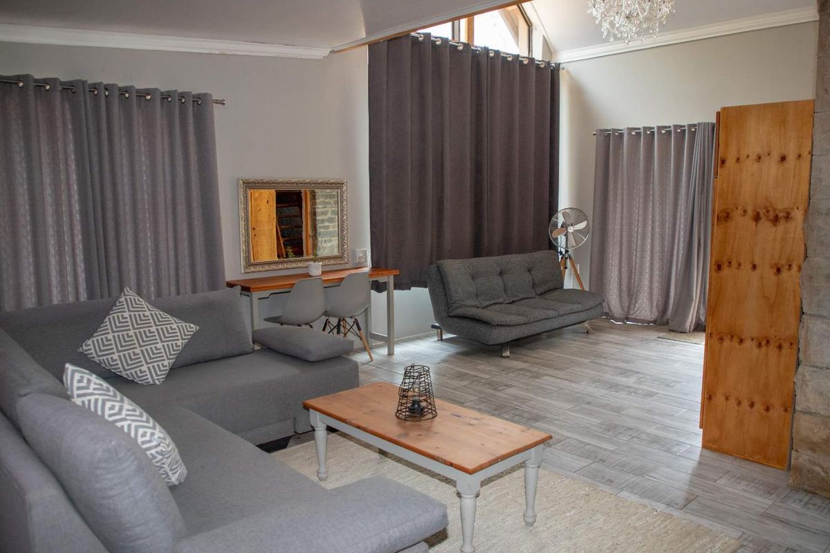 Spacious living room featuring tiled flooring, a vaulted ceiling with recessed lighting, and a stone feature wall, creating a bright and open atmosphere.