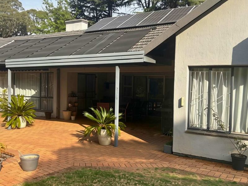 Rear exterior view featuring a covered patio, brick paving, and roof-mounted solar panels on a tiled roof structure.