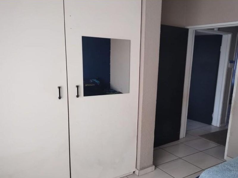 A bedroom interior featuring built-in cupboards with a small inset mirror and tiled flooring, showing signs of wear and tear.