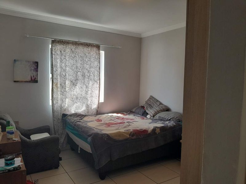A functional bedroom featuring tiled flooring and a window with a curtain rod, offering a neutral space ready for personalization.