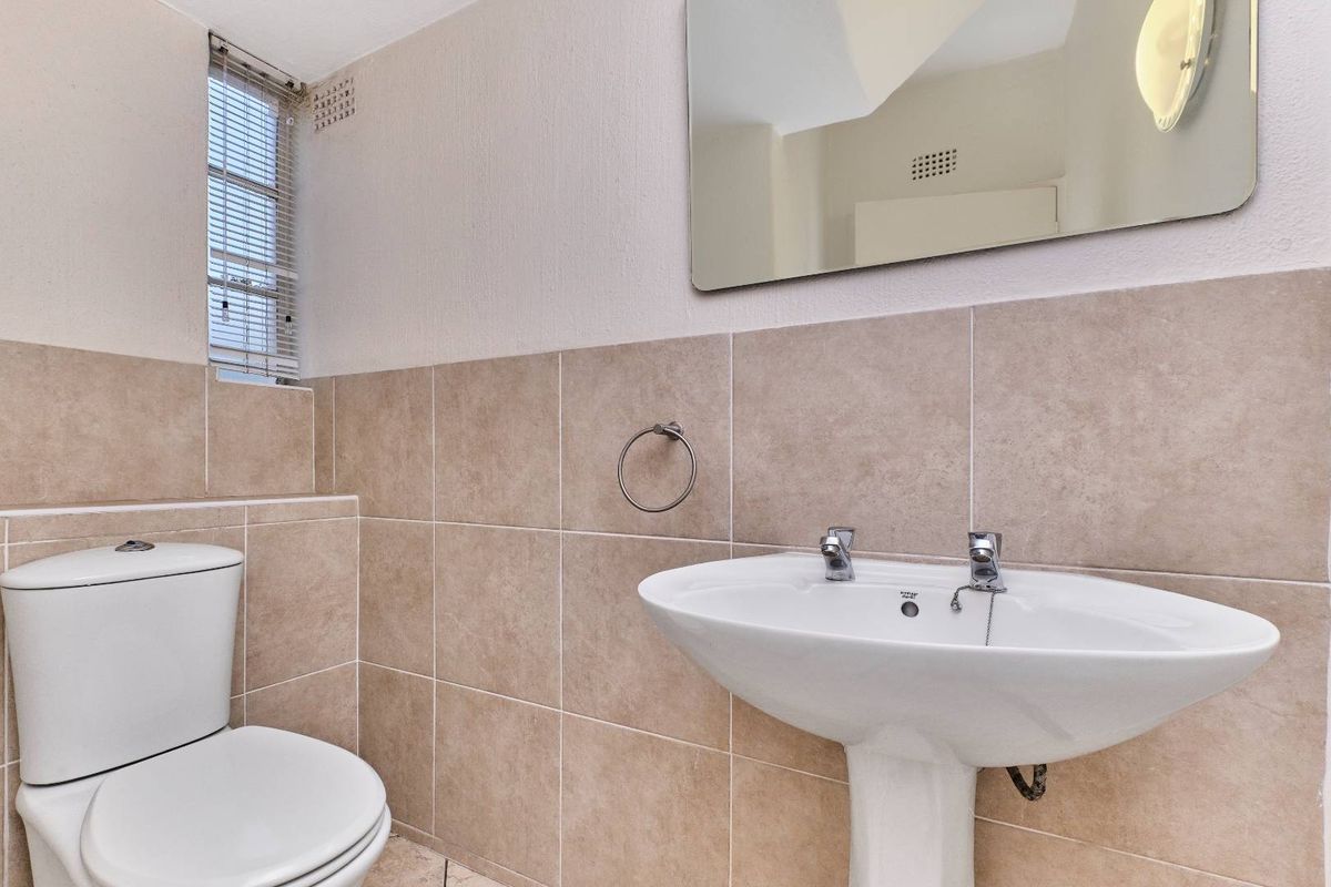 A functional bathroom featuring a pedestal sink, toilet, and neutral wall tiling, providing a clean and practical space.