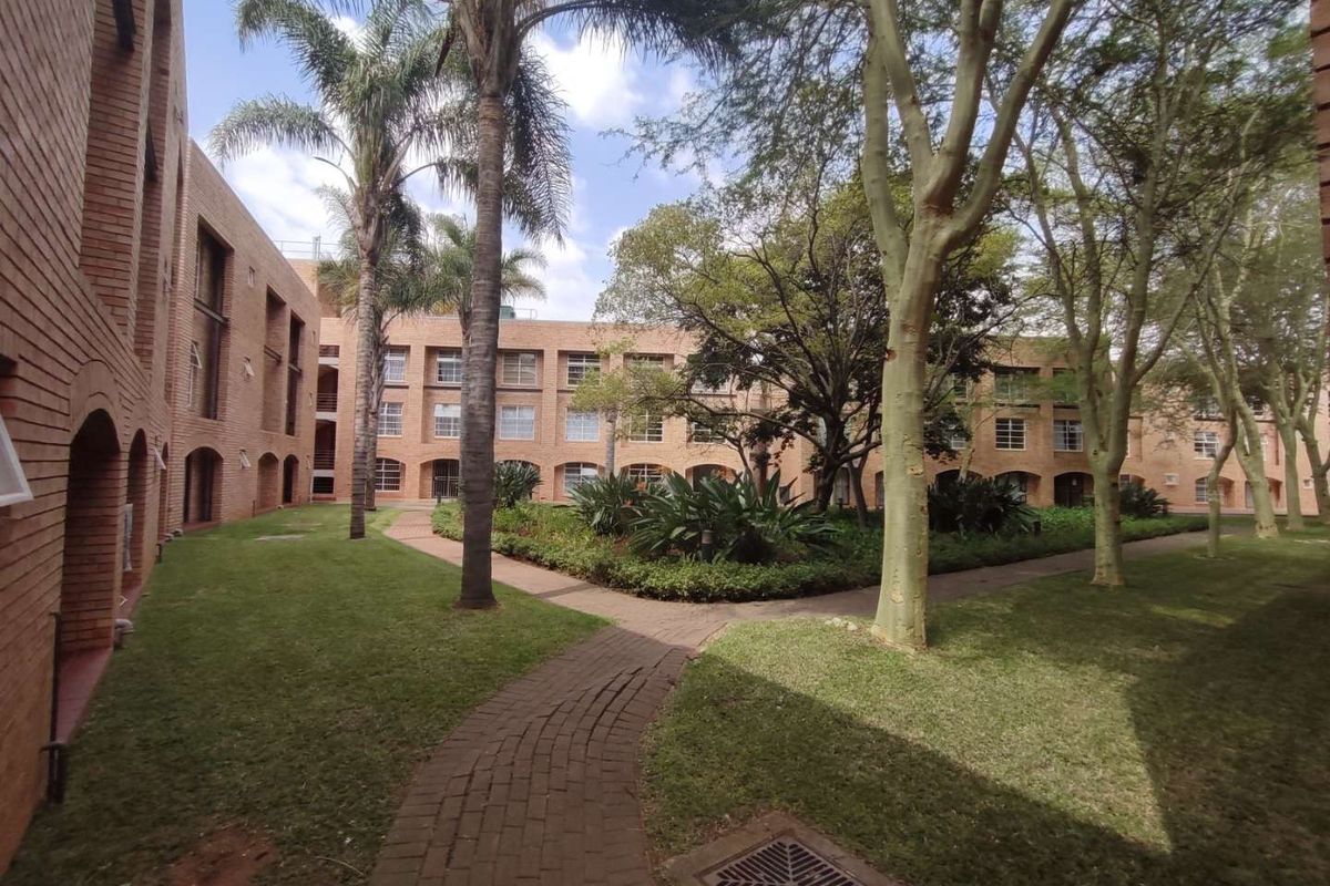 A well-maintained communal garden area featuring brick-faced apartment buildings, mature trees, and paved walkways between the residential blocks.