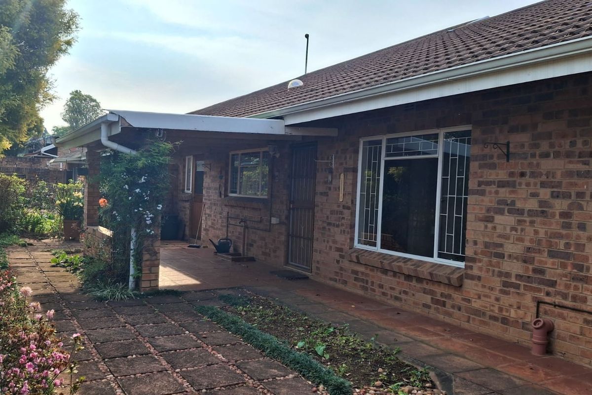 Rear view of the townhouse featuring a face brick facade, a covered patio area, and a paved walkway leading through the garden.