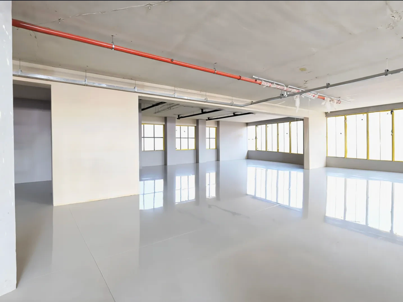 Spacious open-plan retail or commercial area featuring polished concrete floors, large windows for natural light, and exposed industrial ceiling infrastructure.