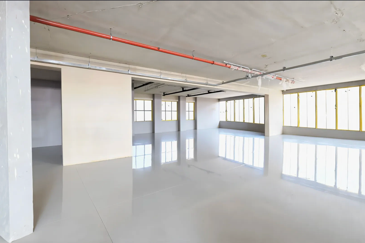 Spacious open-plan retail or commercial area featuring polished concrete floors, large windows for natural light, and exposed industrial ceiling infrastructure.