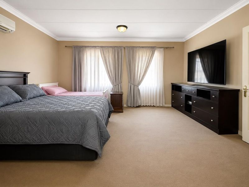 Spacious bedroom featuring neutral wall tones, carpeted flooring, crown molding, and a wall-mounted air conditioning unit.