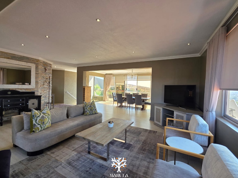 Spacious open-plan living and dining area featuring a stone accent wall, recessed lighting, and large windows providing natural light and scenic views.